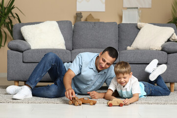 Happy father and his little son playing with wooden cars on floor at home