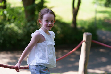 Little cute girl without front tooth rope playground summer park. Concept of active healthy cheerful child