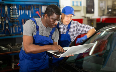 Two auto mechanics diagnosing car engine with laptop with special program at the car repair service center