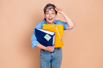 Charming senior woman holding colorful folders with a cheerful expression on beige background