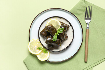 Plate with tasty Dolmas (stuffed grape leaves), lemon slices, napkin and fork on color background