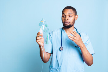 Male nurse doing medical instruction video on how to use handheld nebulizer used for delivering aerosols as treatment. Medic presents inhalation device for lung diseases like pneumonia. © DC Studio
