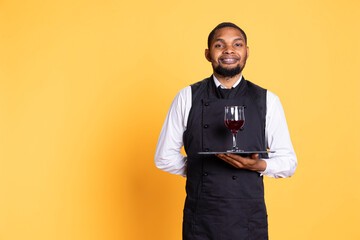 Waiter offering a glass of wine to customers waiting for their food at the table, providing excellent service at a restaurant. Professional staff with uniform bringing drinks to clients.