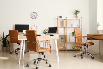 Interior of light office with desks, shelf unit and plants