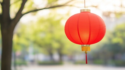 Obraz premium Red chinese paper lantern hanging from a tree in a blurred park background, creating a vibrant, festive atmosphere perfect for chinese new year celebrations