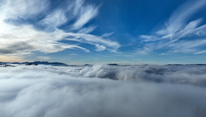 Drohnenaufnahme im Winter mit Nebel im Tal und Sonne im Gebirge
