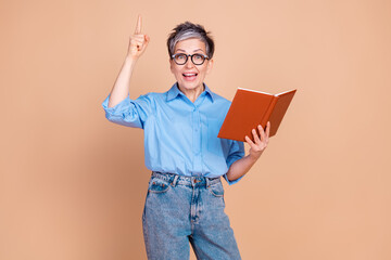 Charming mature woman in casual style holding book and gesturing against beige background