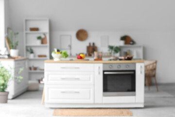 Blurred view of light kitchen with white counters, shelf unit and plants