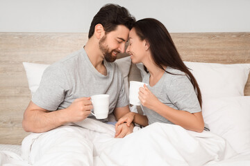 Morning of loving couple with cups of coffee lying in bedroom