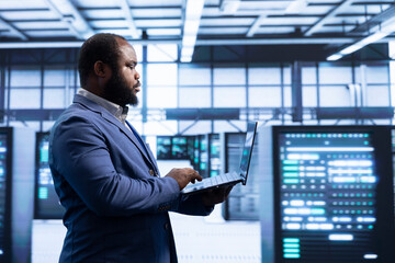 Programmer using laptop in data center with advanced technology, ensuring cybersecurity and...