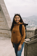 Half length portrait of cheerful asian female traveler in casual wear standing on historical place explore location, smiling woman explorer looking at camera resting on holiday vacations leisure