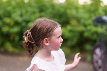 Little girl in a t-shirt standing near cars in a parking lot. Concept of a healthy active cheerful child