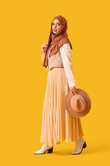 Beautiful Muslim woman in hijab with hat on yellow background