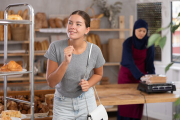 Pleased young girl chooses some bakery goods while Muslim seller works in background in baker's