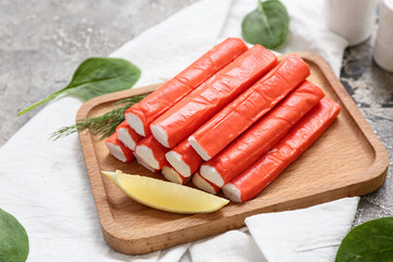 Wooden board with tasty crab sticks, piece of lemon and spinach leaves on grey background © Pixel-Shot