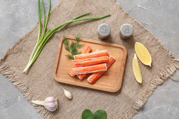 Wooden board with tasty crab sticks, dill, garlic and pieces of lemon on grey background © Pixel-Shot