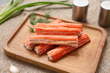 Wooden board with tasty crab sticks and dill on sack cloth background, closeup © Pixel-Shot