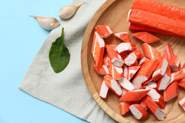 Wooden plate with tasty crab sticks and garlic on blue background © Pixel-Shot
