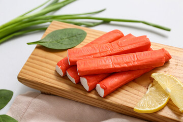 Wooden board with tasty crab sticks, slices of lemon, spinach leaves and green onion on grey background © Pixel-Shot