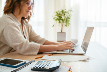 Beautiful middle-aged woman in glasses making marks in financial documents at home office using...