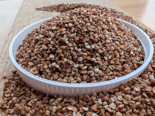 Raw buckwheat in a white bowl on the wooden cutting board. Close up