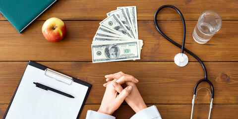 Paid medicine. Money, stethoscope, tablet, female doctor hands on wooden table, top view