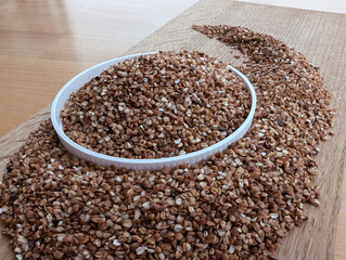 Raw buckwheat in a white bowl on wooden kitchen board