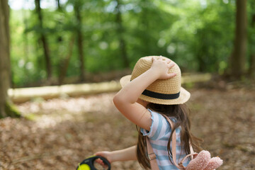 little girl with backpack and straw hat walking in summer park with her back to camera. Children's...