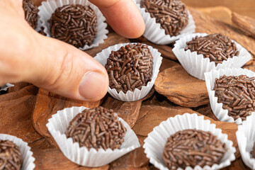 Male hand picking up a Brazilian chocolate truffle over small tree bark_16.