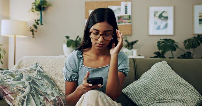 Headache, phone and stress with Indian girl on sofa in living room of home for communication. Annoyed, frustrated or irritated and upset pet owner reading bad news on mobile with dog in apartment