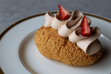 Cake with cream and strawberries on a white plate on a gray background