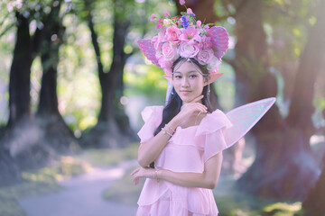 Portrait fantasy Angel Fairy Tale woman in forest natural trees. Elf girl fashion in pink dress with butterfly wings fairy tale story world. Walks in fresh green trees with magic radiance.