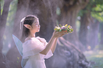 Portrait fantasy Angel Fairy Tale woman in forest natural trees. Elf girl fashion in pink dress with butterfly wings fairy tale story world. Walks in fresh green trees with magic radiance.