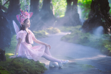 Portrait fantasy Angel Fairy Tale woman in forest natural trees. Elf girl fashion in pink dress with butterfly wings fairy tale story world. Walks in fresh green trees with magic radiance.