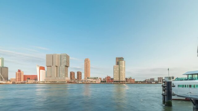 Panorama showing Rotterdam skyline timelapse from Nieuwe Maas River bank to Wilhelminapier and Kop van Zuid. Modern skyscrapers, ferry station and Erasmus Bridge, waterfront with boats passing by