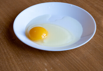 Raw chicken egg in a white dish on the table