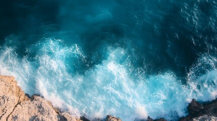 Fototapeta premium Aerial view of turquoise ocean waves crashing against rocky shore.