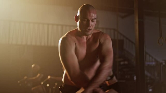 Fit sportsman with nude torso jumping over skipping rope in slow-motion while people riding stationary bike in the background