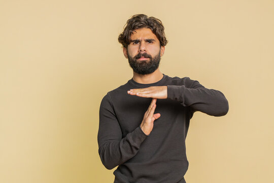 Tired serious upset young Lebanese man showing timeout gesture, limit or stop sign, no pressure, I need more time, relax, break deadline. Indian Hindu guy isolated on studio beige background indoors.