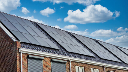 Fototapeta premium Newly build houses with solar panels attached on the roof against a sunny sky