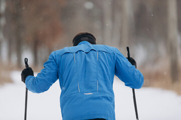 Back view of a male skier athlete skiing uphill on a cross-country trail