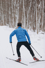 Back view of a male skier athlete skiing uphill on a cross-country trail