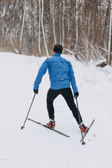 Back view of a male skier athlete skiing uphill on a cross-country trail