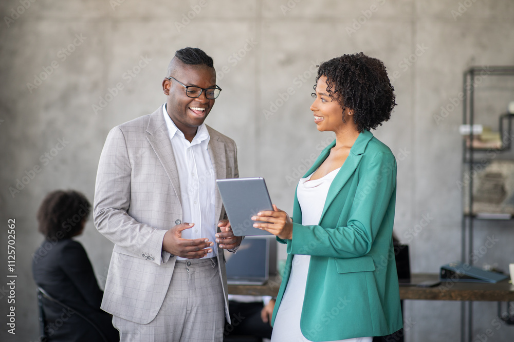 Poster two professionals engage in a discussion while reviewing a digital tablet in a contemporary office. 