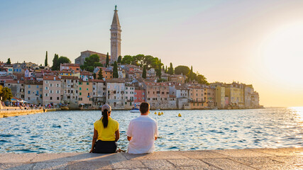 Two friends relax by the Adriatic Sea, enjoying the stunning sunset over Rovinj Croatia charming waterfront and colorful buildings, embracing a serene moment of tranquility and connection.