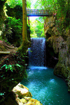 Heavenly view from Pioraco at a waterfall of the Potenza River in Sentiero Li Vurgacci, glowing green blue waters cascading from above and creating foam below, in the Sibillini Mountains, and a bridge
