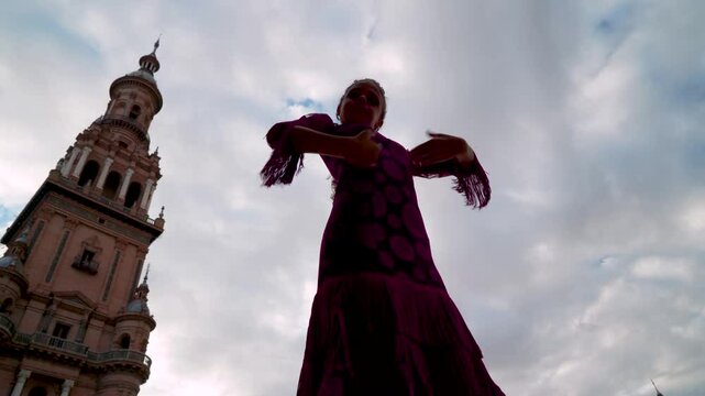 Ni&ntilde;a t&iacute;pica espa&ntilde;ola bailando flamenco con el luminoso cielo con nubes al fondo dibujando su silueta, desde la ciudad de Sevilla, Andaluc&iacute;a, Espa&ntilde;a.