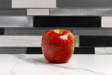 A Honeycrisp apple on white marble kitchen countertop with a multi-tone tile backsplash behind in the backdrop.
