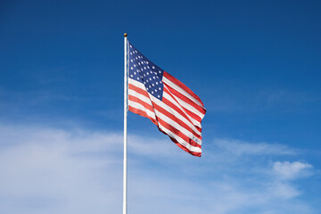 Large American Flag waving on a sunny and bright blue sky with cirrostratus clouds in the background.