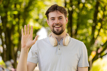 Hello, welcome. Athletic fit runner guy waving hi with palm greeting with hospitable friendly smile. Young Caucasian man jogger workout cardio training in park at morning. Active healthy sportsman. © Andrii Iemelianenko